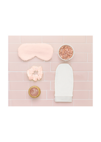 Spa essentials including sherpa eye mask, exfoliator mitt, pink salt, silky scrunchie, and massager displayed on pastel tiles.