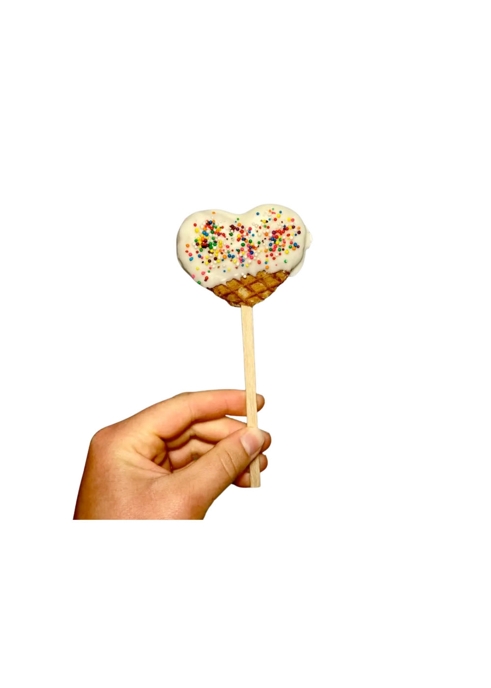  Hand holding a heart-shaped white chocolate-covered waffle on a stick with colorful sprinkles.