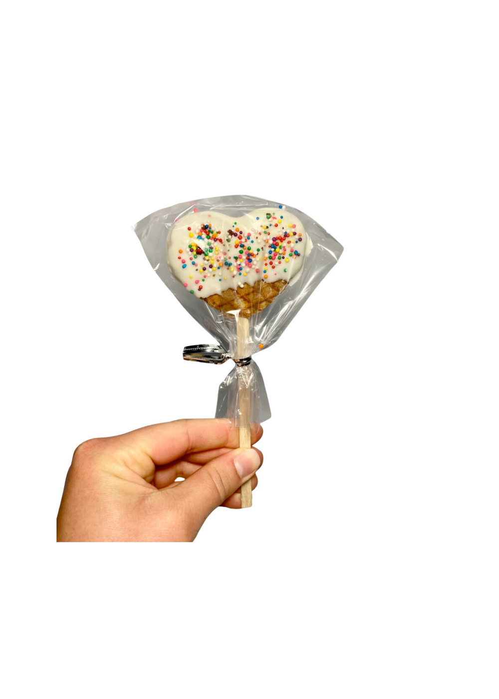 Hand holding a packaged heart-shaped white chocolate-covered waffle on a stick with colorful sprinkles.