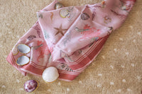 Pink silk scarf with seashell and marine motifs, accompanied by seashell compacts, ideal for beach fashion inspiration.