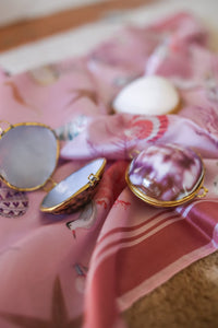 Pink silk scarf with seashell and marine motifs, accompanied by seashell compacts, ideal for beach fashion inspiration.