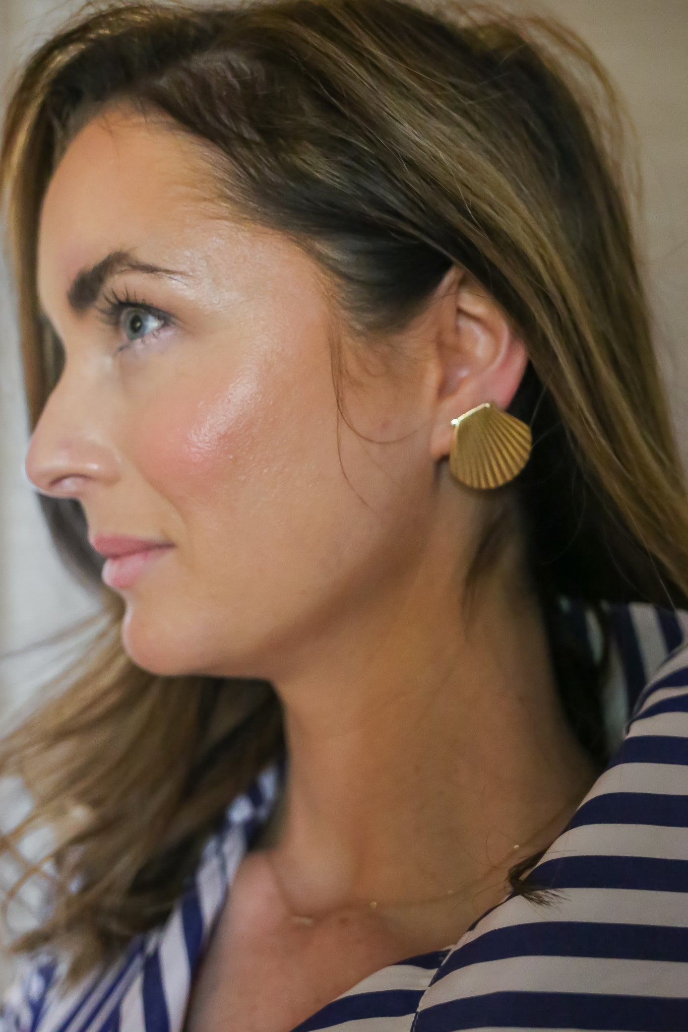 Profile View of Woman Wearing Gold Shell Earrings and Striped Shirt: A profile shot of a woman wearing large gold shell earrings paired with a blue-and-white striped shirt, highlighting her elegant accessory choice.