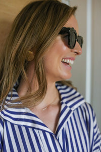 Profile View of Woman Wearing Gold Shell Earrings and Striped Shirt: A profile shot of a woman wearing large gold shell earrings paired with a blue-and-white striped shirt, highlighting her elegant accessory choice.