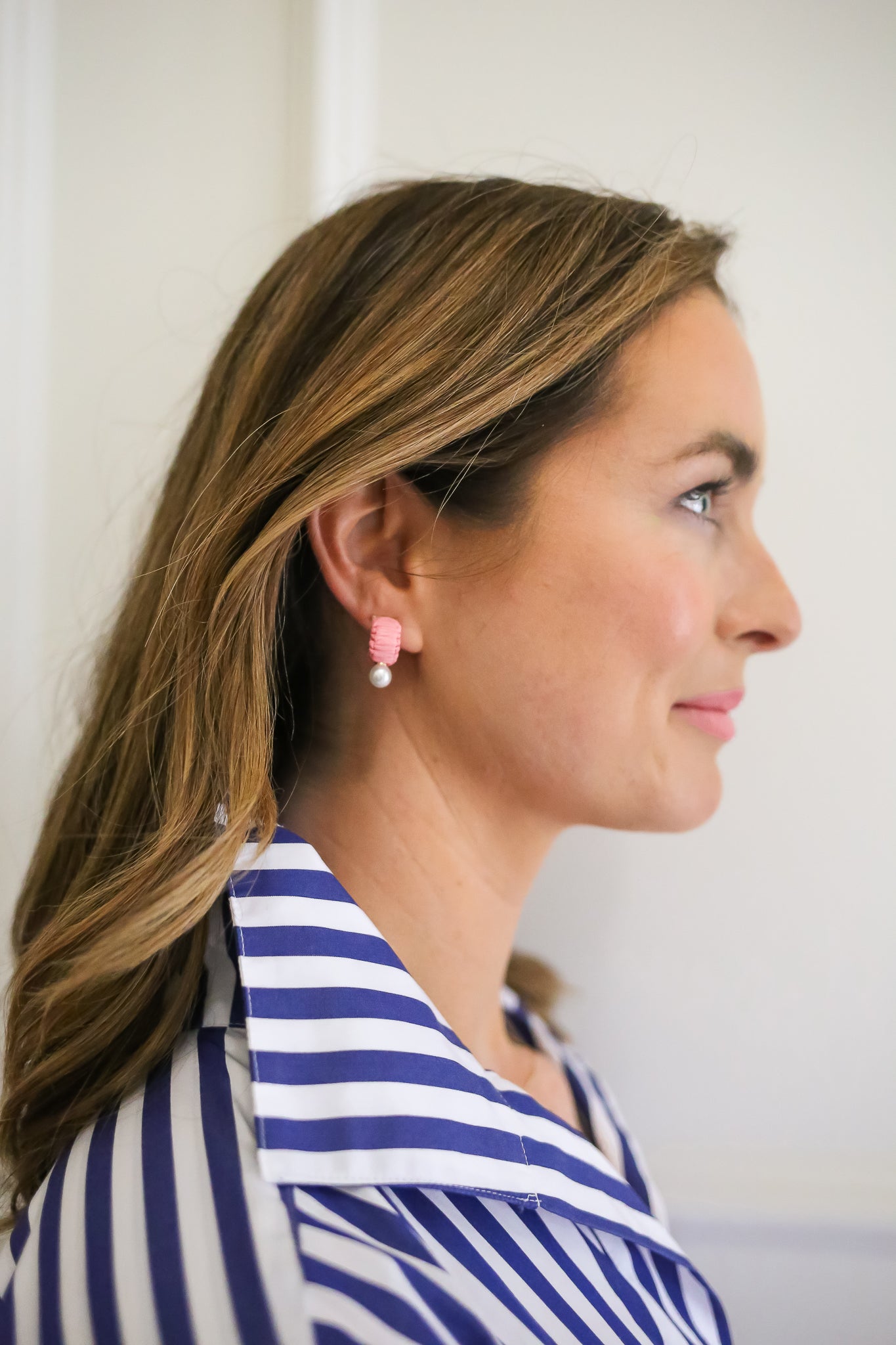 Profile of Woman Wearing Pink and Pearl Earrings: A woman in a blue-and-white striped shirt wears small pink and pearl earrings, creating a look that blends preppy style with feminine charm.